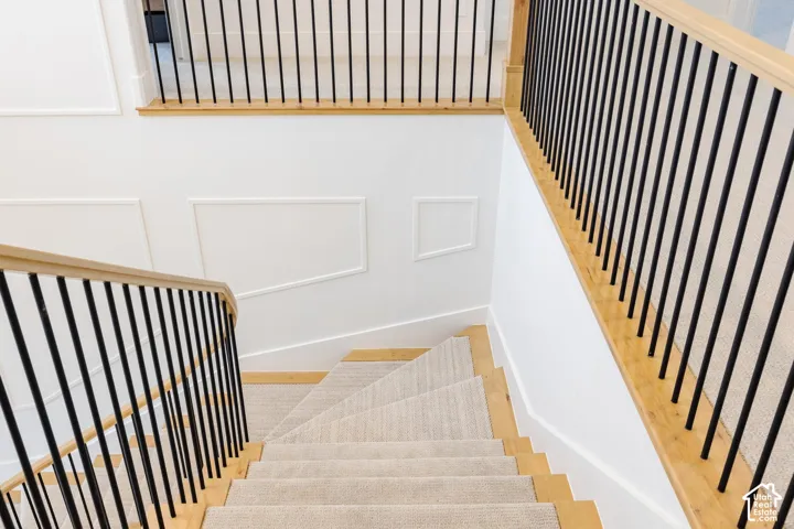 Staircase featuring wood-finish treads, light-toned carpet runner, and contemporary black metal balusters