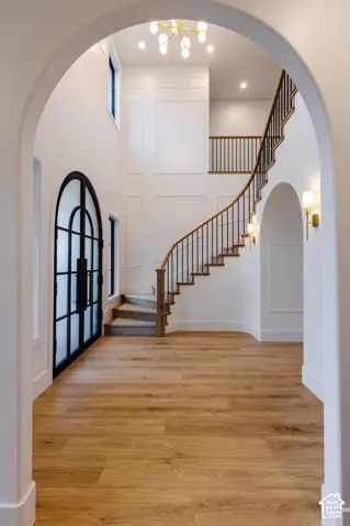 Grand entryway featuring a curved staircase with wood handrails and black metal balusters, wood-finish flooring, a two-story arched window with black framing, and a contemporary gold-finish chandelier