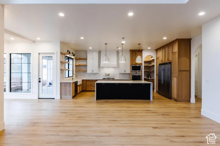 Open-concept kitchen featuring light wood-finish flooring, a central island with a black base, and a mix of light and dark wood cabinetry