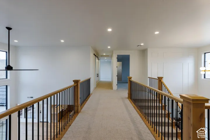 Carpeted hallway featuring wood newel posts with black metal balusters, recessed lighting, and a modern ceiling fan