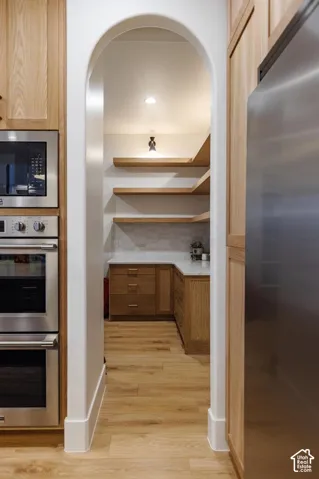 Archway entrance to a pantry featuring wood-finish flooring, recessed lighting, floating wood shelving, wood cabinetry, and stainless steel appliances