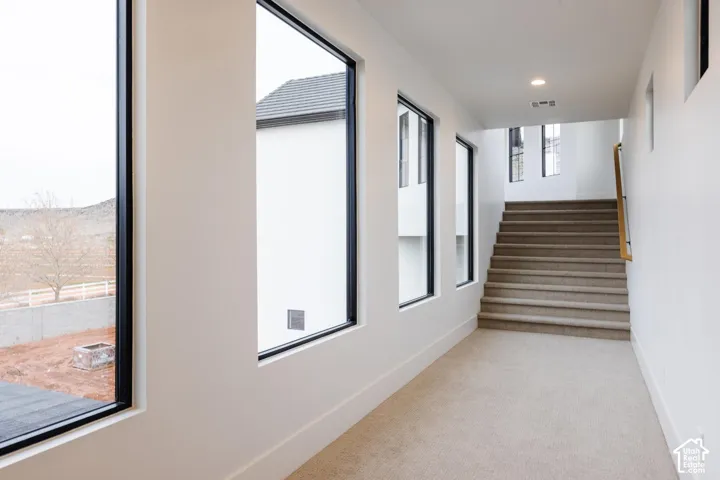 Carpeted hallway with a staircase featuring a wood handrail