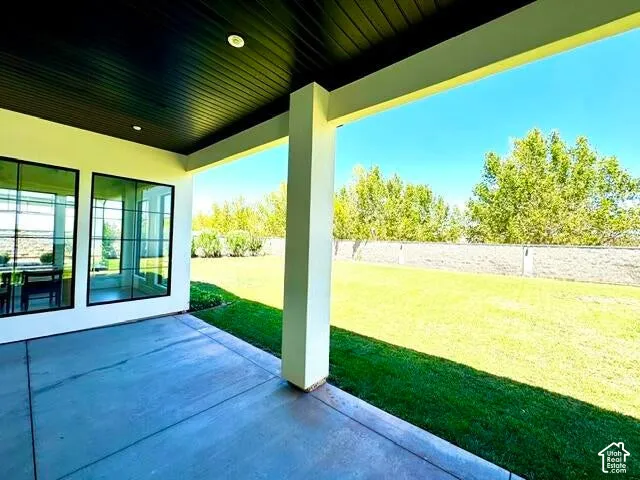 Covered patio with concrete flooring, recessed lighting, expansive green lawn, and a block wall perimeter