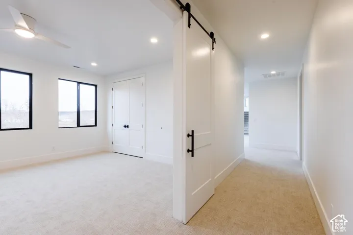 Bright room with light-toned carpeting, featuring two large windows with black frames, a double-door closet with dark hardware, and a ceiling fan with integrated lighting