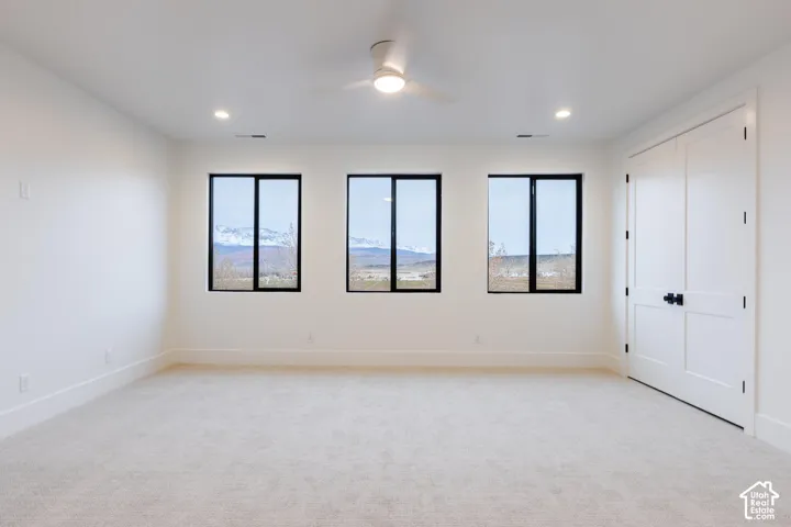 Bright room featuring three large windows with mountain scenery, neutral carpet, a contemporary ceiling fan, recessed lighting, and double bi-fold doors with black hardware