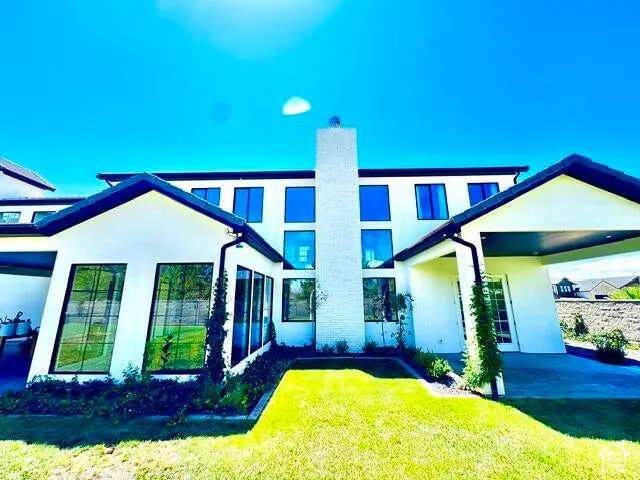 Contemporary exterior featuring a bright white facade, a prominent central chimney, large black-framed windows, dark rooflines, and a covered entryway