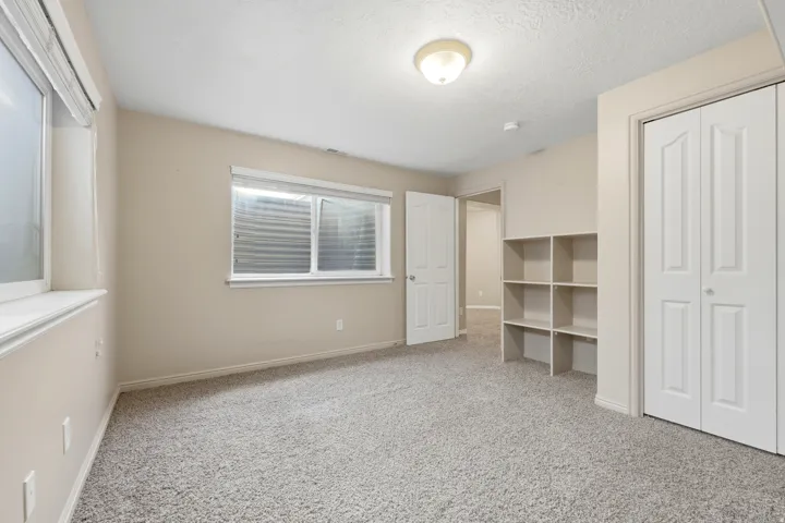 Carpeted room featuring two windows, recessed built-in shelving, a full door, a bi-fold closet door, and a ceiling-mounted light fixture