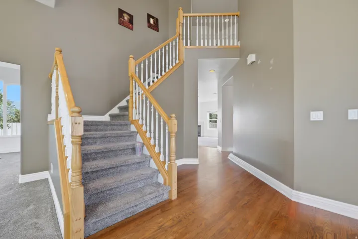 Two-story foyer featuring a carpeted staircase with wood banisters, hardwood flooring, and neutral wall tones