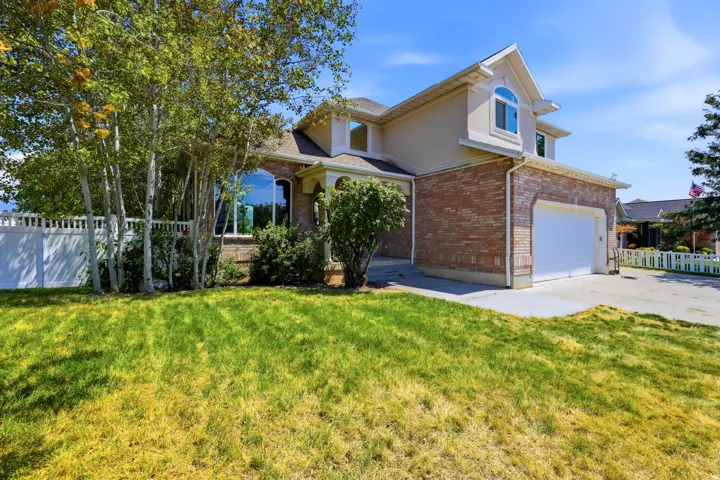 Brick and stucco exterior featuring an arched entryway, two-car garage, and mature landscaping