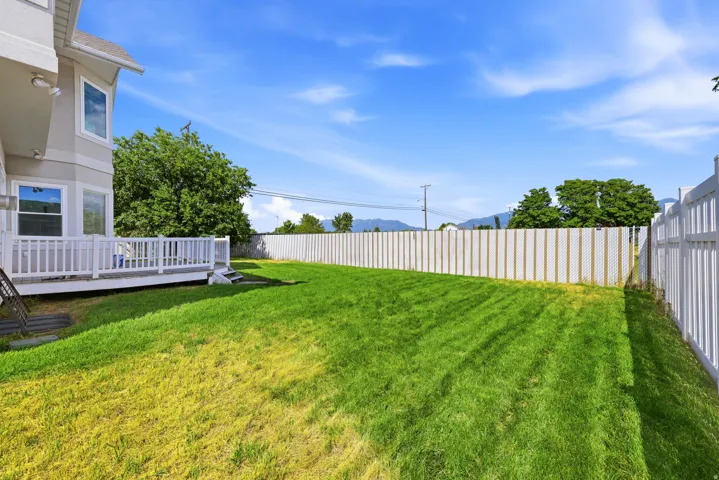 Expansive backyard featuring a large green lawn, full white privacy fence, and a white wooden deck with steps