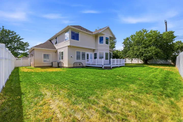 Expansive backyard featuring a large green lawn, a white privacy fence, and a multi-level deck with white railings