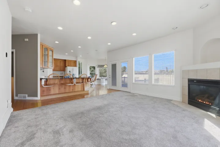 Spacious open-concept living area featuring light gray carpeting, a tile-surround fireplace, and recessed lighting