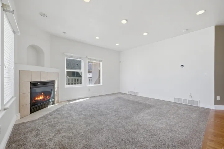 Spacious interior room featuring a corner fireplace with a tile surround and hearth, recessed ceiling lighting, light gray carpet, and multiple windows with blinds