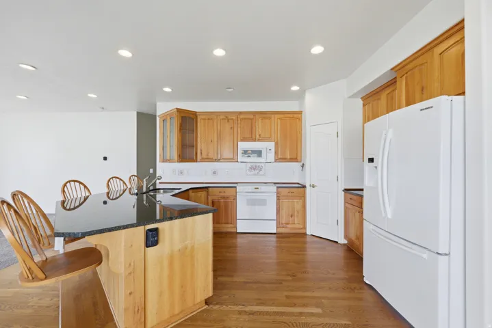Kitchen with wood-finish flooring, recessed lighting, and a large central island featuring a dark countertop and integrated sink