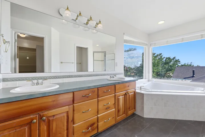 Bathroom featuring a built-in soaking tub, a dual vanity with light wood cabinetry, and a large mirror