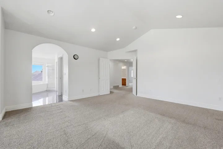 Spacious room featuring neutral carpeting, recessed lighting, and an arched entry to an adjoining tiled space with a window