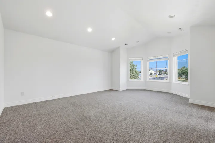 Room featuring a bay window, vaulted ceiling, recessed lighting, neutral carpet, and white baseboards