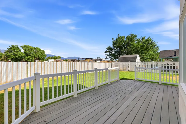 Expansive outdoor deck featuring composite decking, white railing, and a fenced backyard with a detached shed and mature trees