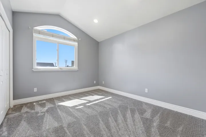 Arched window with broad sills, vaulted ceiling with recessed lighting, paneled bi-fold closet doors, contemporary gray walls, and patterned carpet flooring
