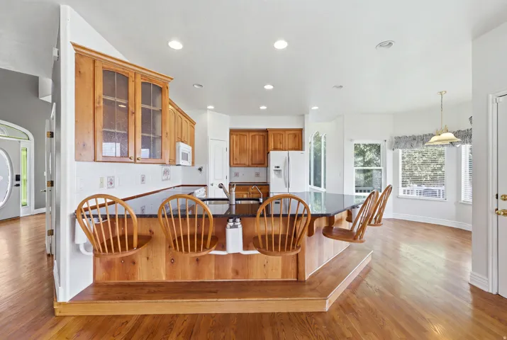 Spacious kitchen featuring a breakfast bar with built-in seating, wood-finish flooring, a white tile backsplash, and light wood cabinetry