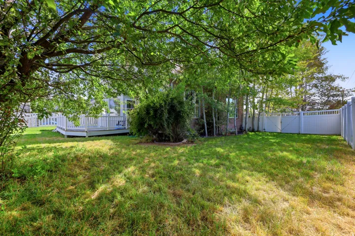Expansive lawn area featuring a white privacy fence, mature trees, and a wooden deck with baluster railing