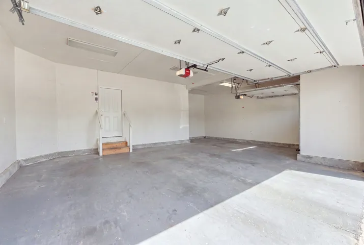 Spacious three-car garage featuring a concrete floor, white painted walls, and overhead fluorescent lighting