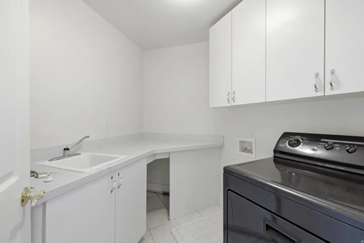 Laundry area featuring white cabinetry, a built-in utility sink, light-toned countertops, and white tile flooring