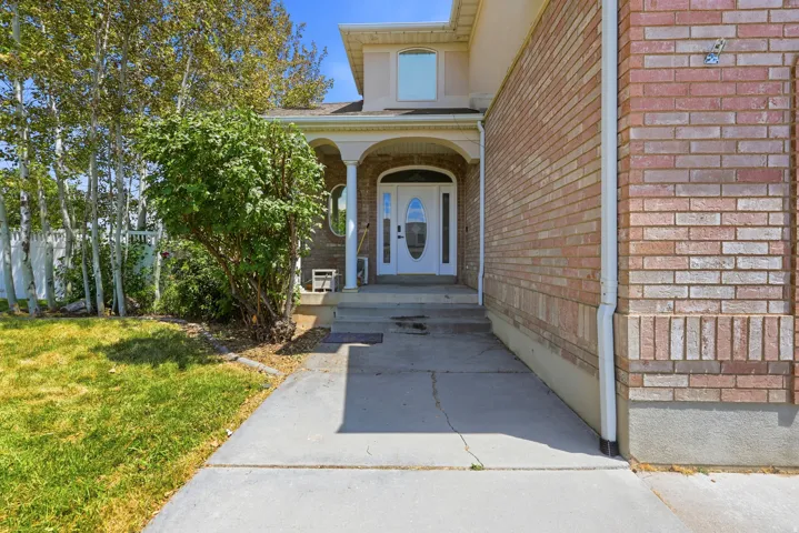 Brick exterior featuring a covered entry, white door with decorative glass, and concrete walkway