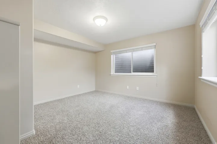 Neutral-toned room featuring a single window with blinds, light beige walls, and plush carpet flooring