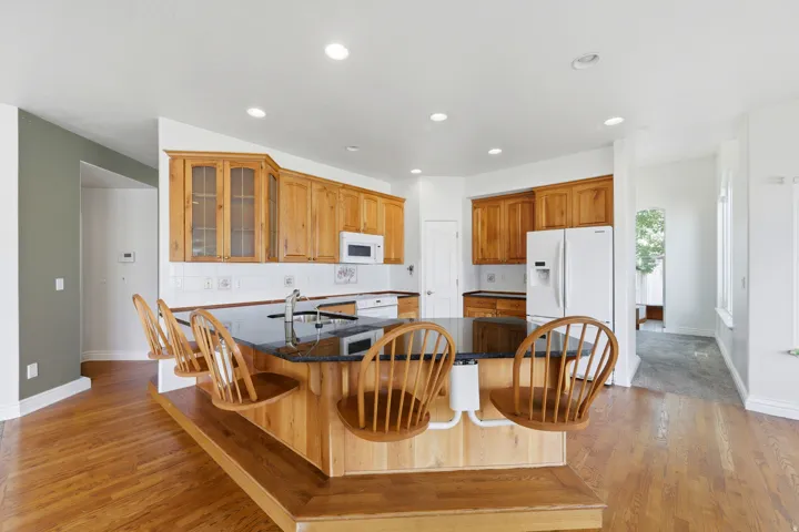 Kitchen featuring wood cabinetry, a large central island with seating, a black countertop, and wood-finish flooring