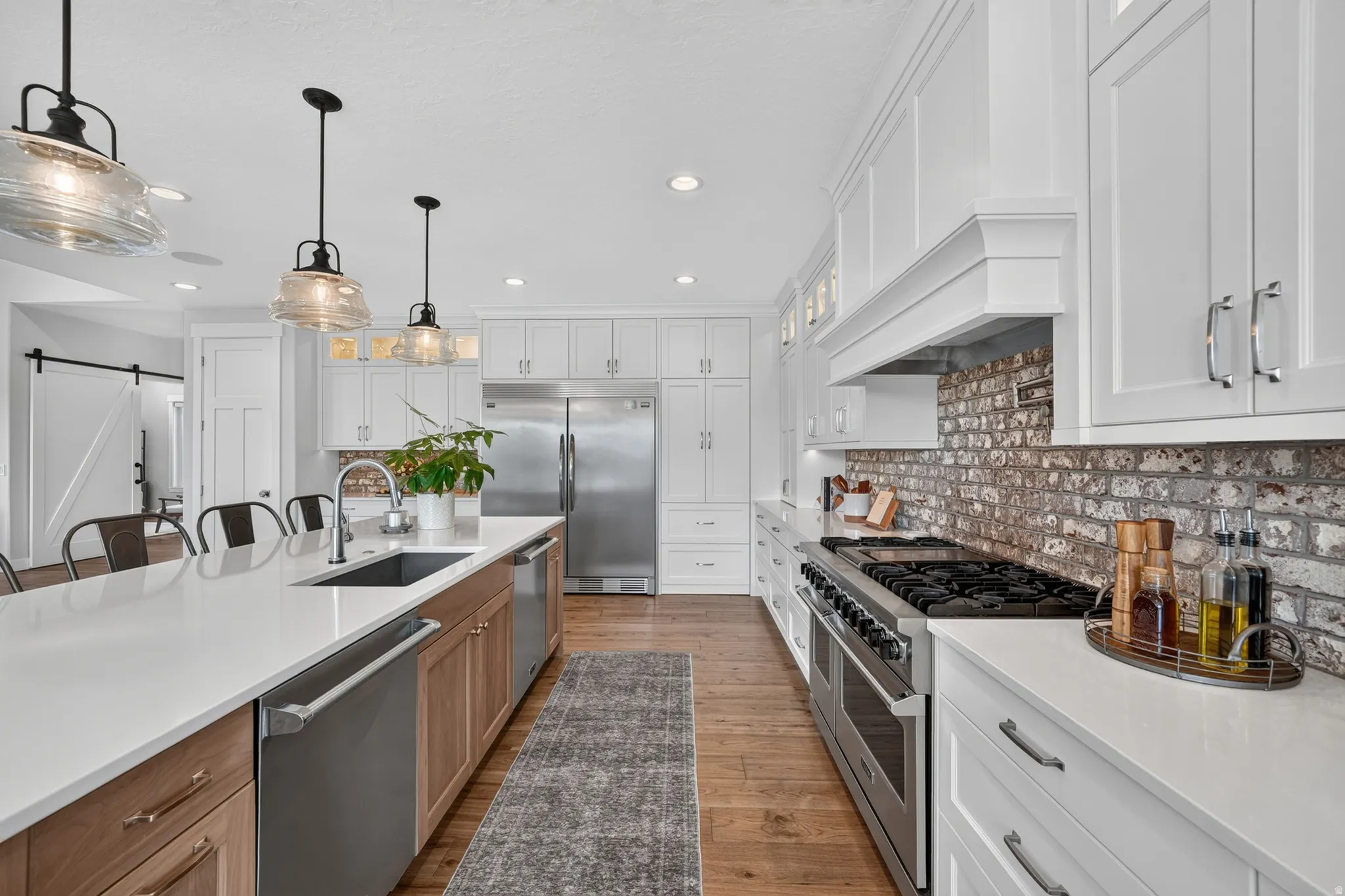 Gourmet kitchen featuring a substantial island with seating, stainless steel appliances, white shaker cabinetry, a brick-style backsplash, and wood-finish flooring