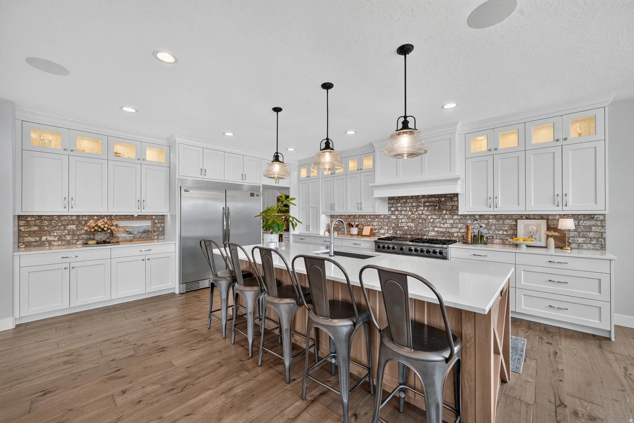 Gourmet kitchen featuring a substantial island with seating, a large range with hood, white cabinetry, brick-finish backsplash, and wood-finish flooring