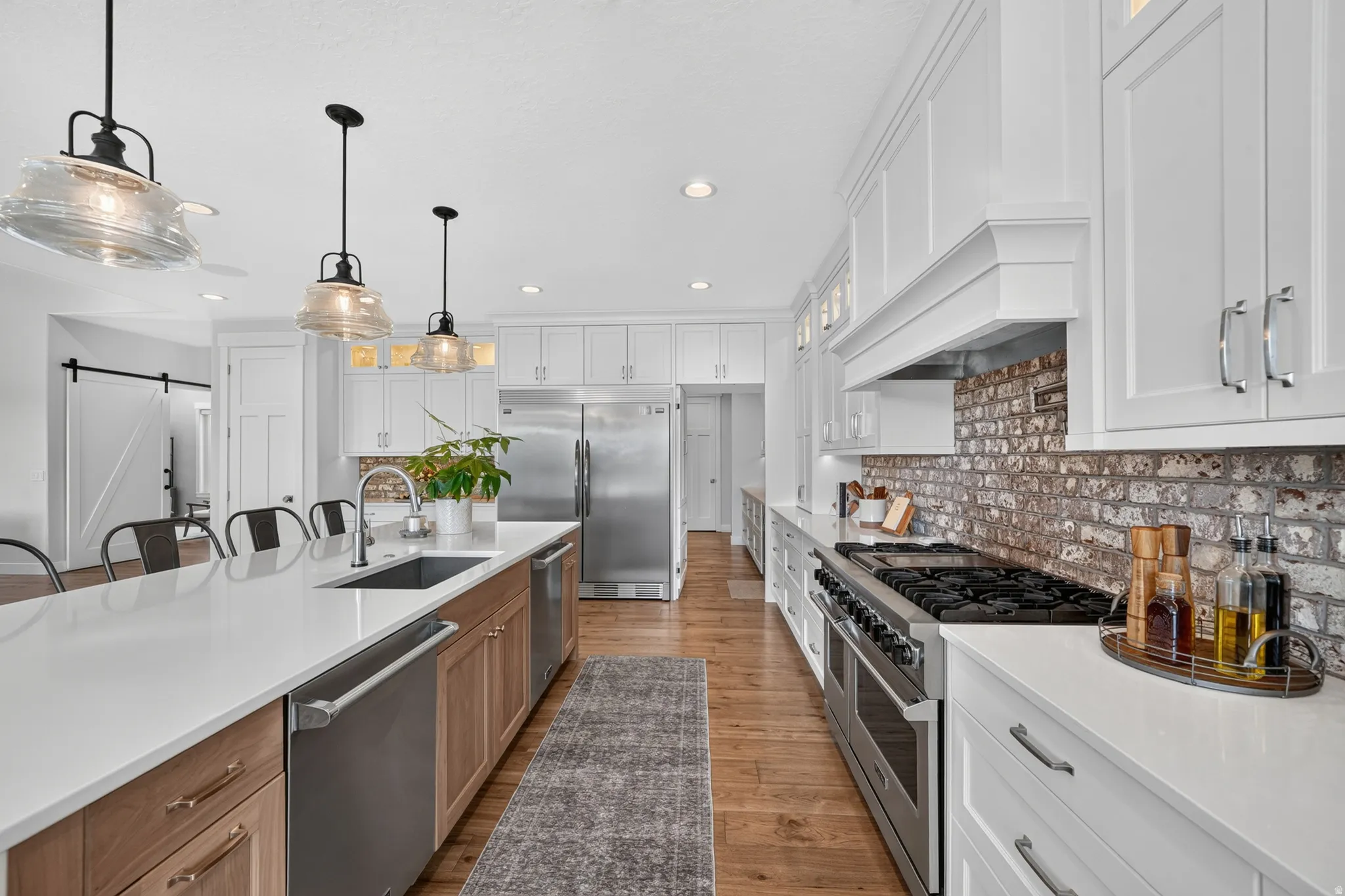 Gourmet kitchen featuring a large island with an undermount sink, white countertops, wood-finish flooring, white upper cabinetry, and a brick backsplash