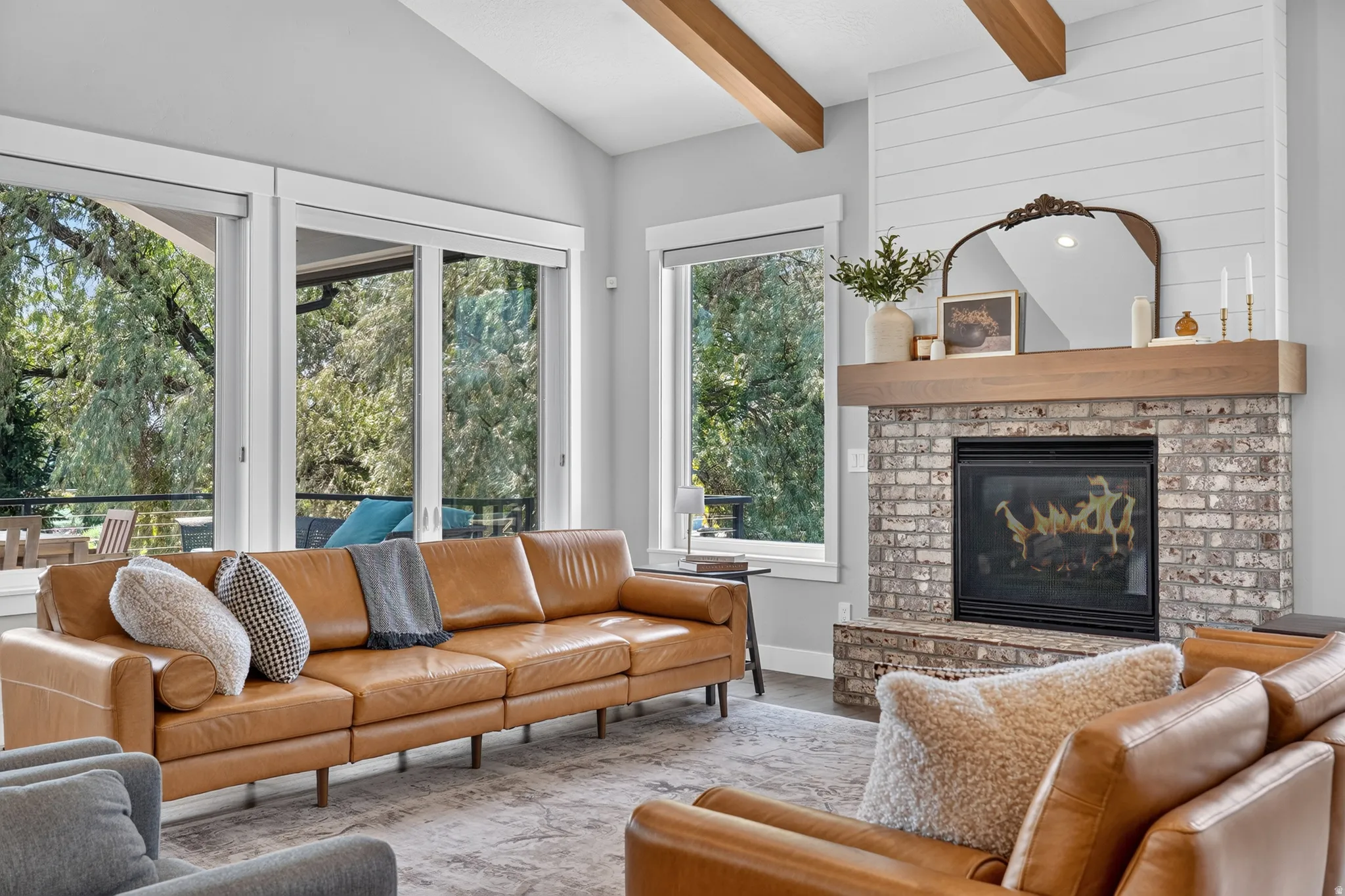 Spacious living area featuring a brick fireplace with a wood mantle, white shiplap accent wall, and exposed wood ceiling beams