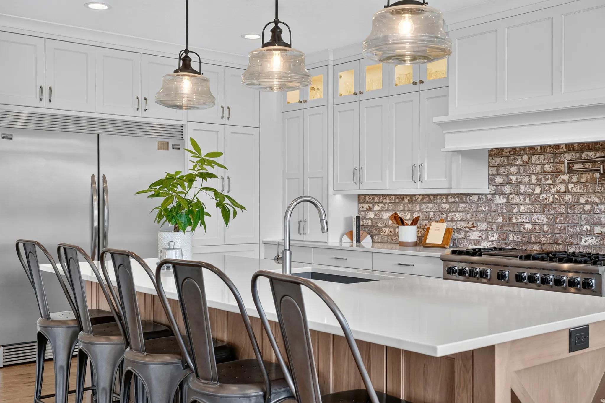 Kitchen featuring a large central island with seating, white shaker cabinetry, stainless steel appliances, a range hood, and a brick-look backsplash
