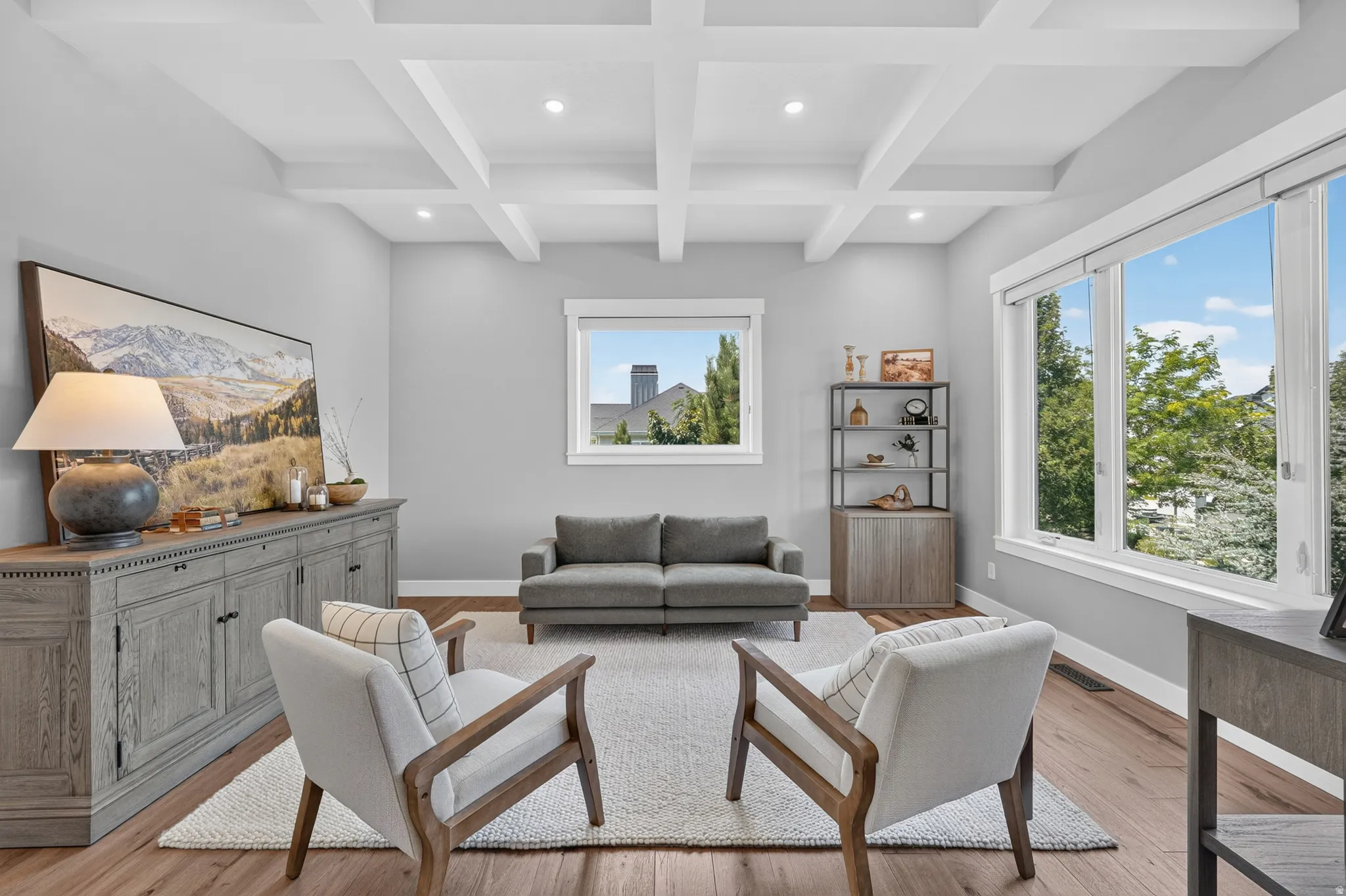 Coffered ceilings complement wood-finish flooring in this bright interior space, featuring large windows with white trim and recessed lighting