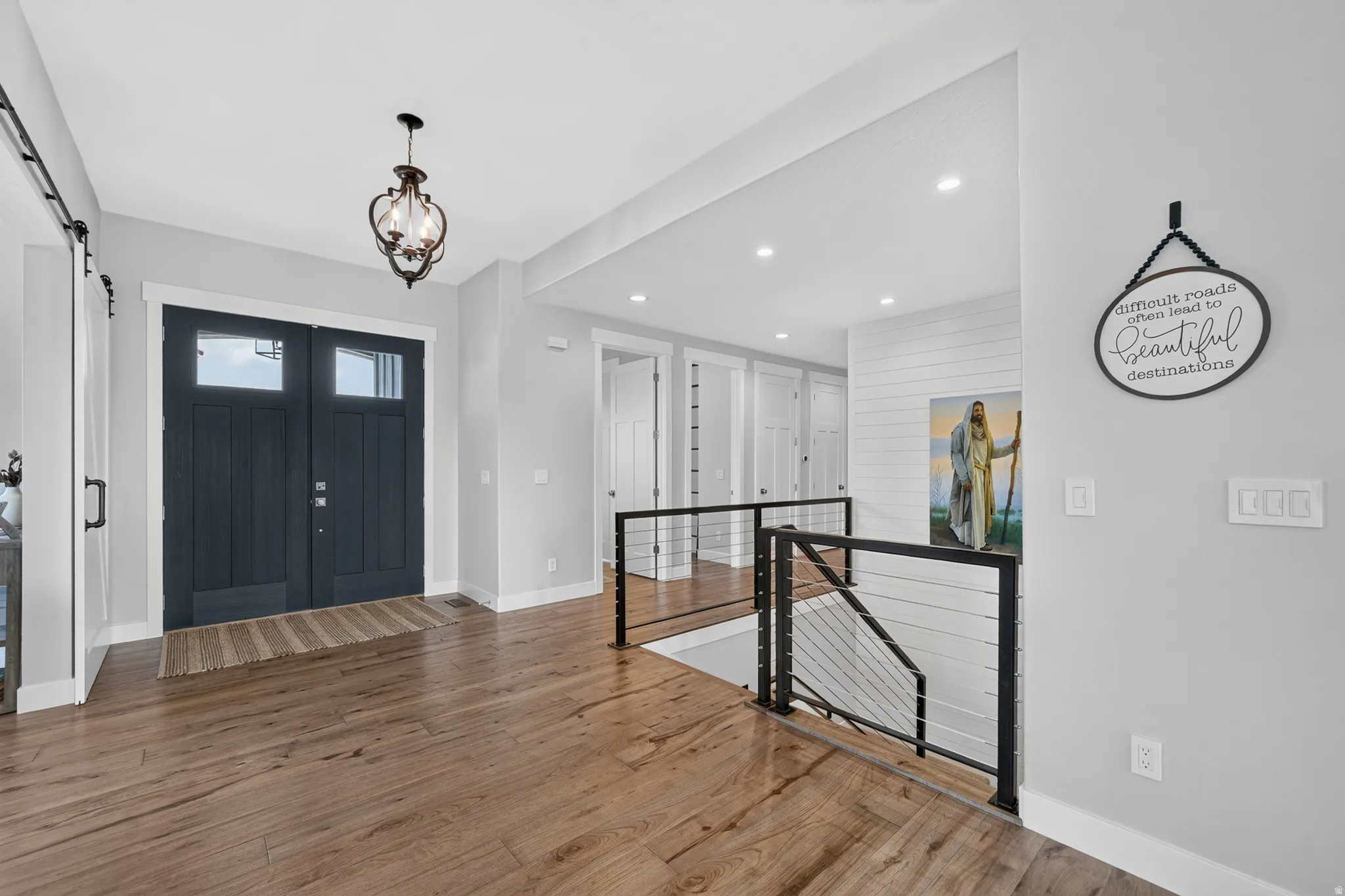 Entryway featuring a dark paneled double door with glass inserts, wood-finish flooring, a decorative chandelier, and a contemporary cable railing system