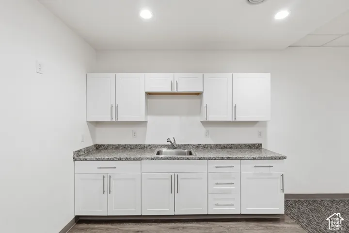 White shaker-style cabinetry with brushed nickel hardware, gray speckled countertop, stainless steel sink, and wood-finish flooring