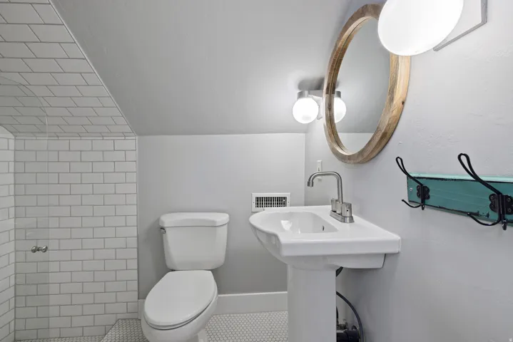 Bathroom featuring a pedestal sink with a brushed nickel faucet, a round wood-framed mirror, and a wall-mounted light fixture