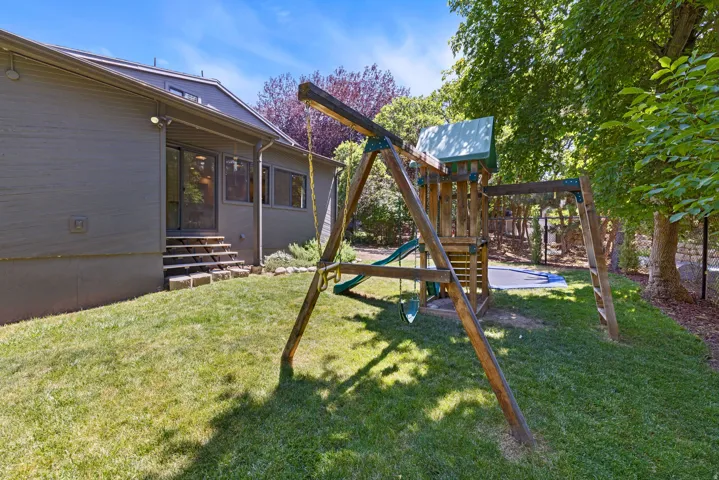 Expansive green lawn with mature trees and a wooden play structure