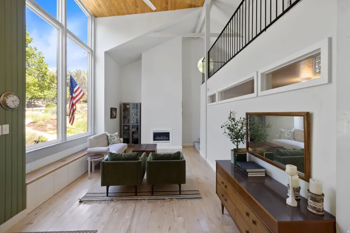 Two-story living area featuring a vaulted wood-finish ceiling, expansive floor-to-ceiling windows, light wood-finish flooring, and a built-in fireplace