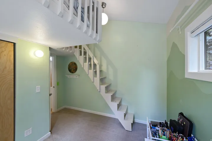 Carpeted room featuring a white wooden staircase leading to an overhead loft bed with a matching white railing
