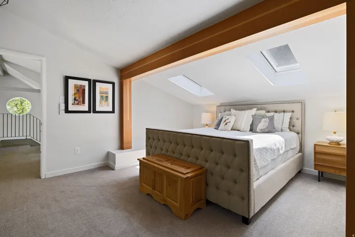 Primary bedroom featuring vaulted ceilings, exposed wood beams, and multiple skylights