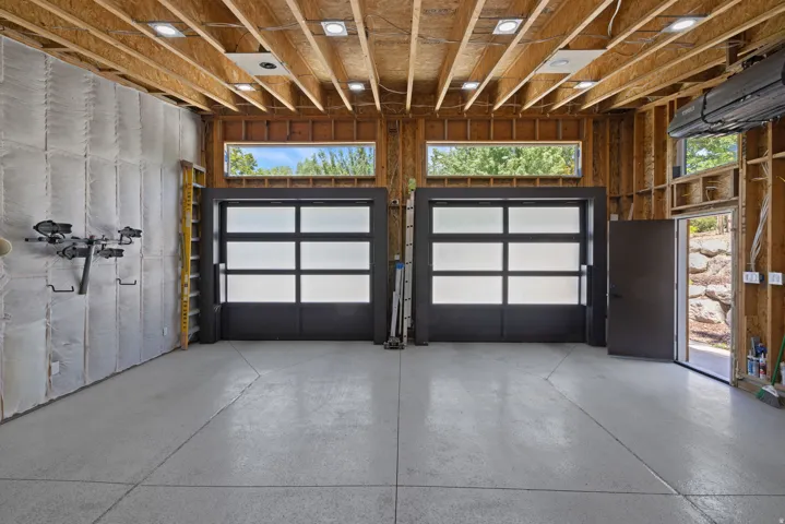Spacious garage featuring two modern frosted-panel garage doors, high ceilings with exposed wood beams, and recessed lighting