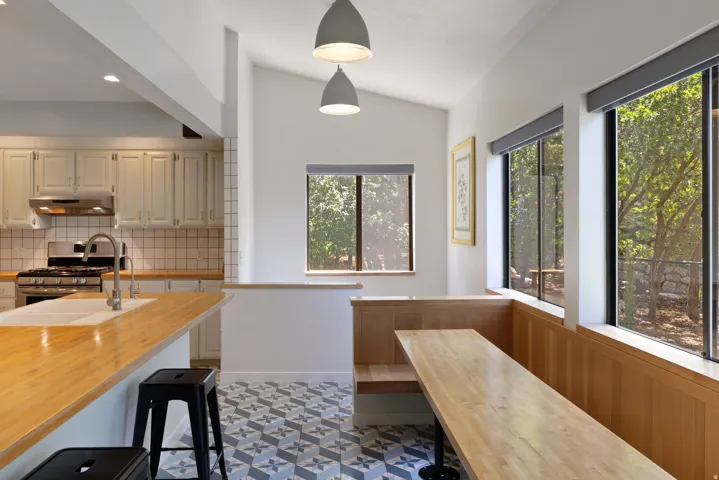 Kitchen and dining area featuring a vaulted ceiling with pendant lighting, wood-finish countertops, custom built-in bench seating, geometric floor tiling, and multiple windows