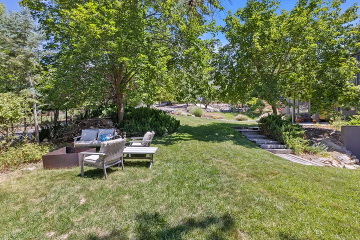Expansive lawn area featuring mature trees, a built-in metal fire pit, and terraced landscaping