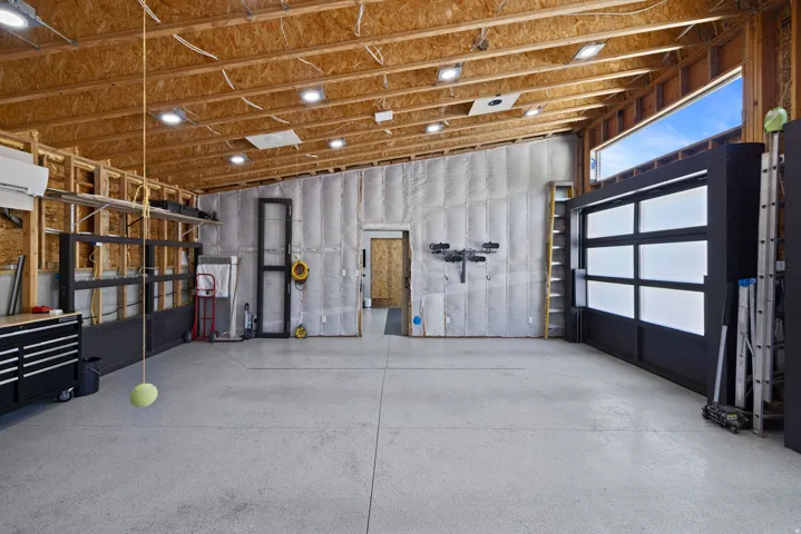 Spacious garage featuring exposed wood beam ceilings with recessed lighting, an epoxy-coated concrete floor, and a modern roll-up door with frosted panels
