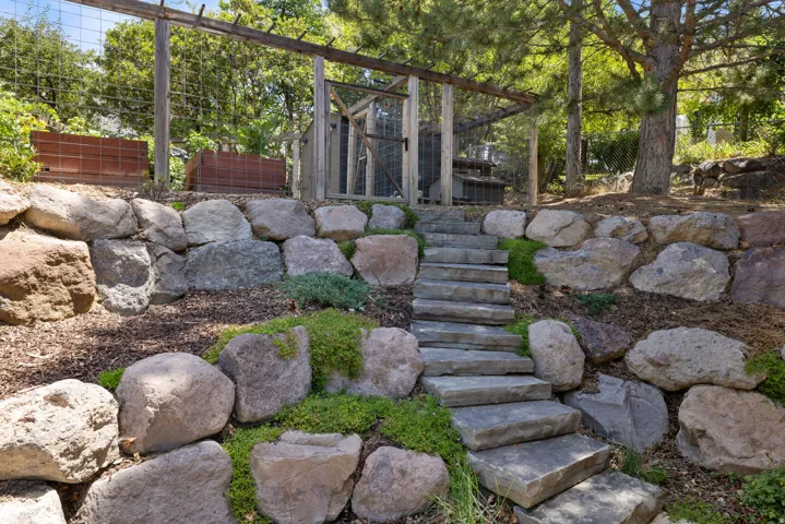 Stone steps ascending a terraced landscape featuring large boulder retaining walls, integrated plantings, and wood mulch