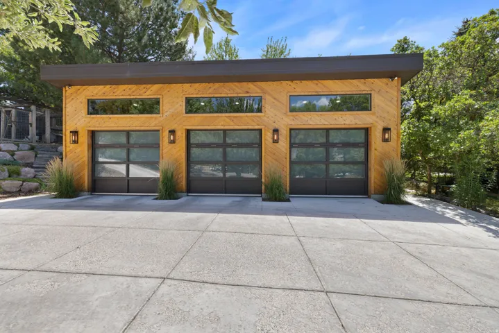Modern garage structure featuring three glass-paneled doors, wood-finish siding, and a flat roofline