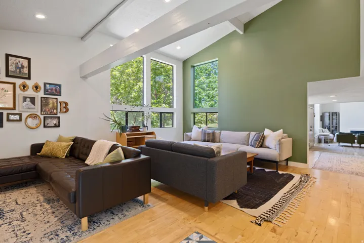 Vaulted ceiling living space featuring exposed white beams, recessed lighting, large windows, and light wood-finish flooring